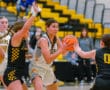 Girls' high school basketball game, player in white holds ball while being defended by two players in black uniforms.