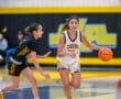 High school girls basketball game action, player in white jersey dribbling past defender on court.
