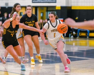 Basketball game action with player dribbling past defender in gymnasium.