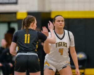 Two female basketball players in action during a game, one in a Tigers uniform and the other wearing number 11.