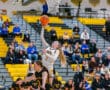 High school basketball player jumps for a layup shot in a game, with spectators in the background.