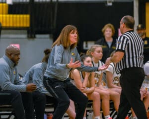 Basketball coach passionately discusses with referee during a game beside focused team members on the bench.