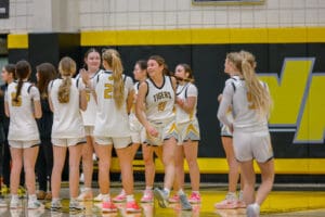 High school girls' basketball team in white uniforms huddling on the court.