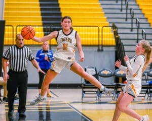 Basketball player in mid-air action, avoiding opponent during a game in a yellow and black home stadium.