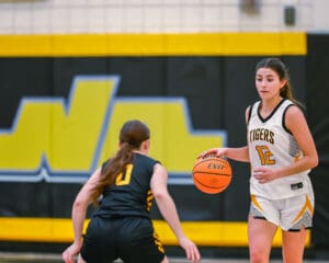 Two basketball players in action, one dribbling the ball, wearing white, against an opponent in black on the court.