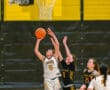 Girls' basketball game action with player jumping to score near the hoop, opponents attempting to block.