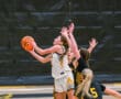Girls' basketball game action, player in white jersey attempts a layup against defenders in black uniforms.