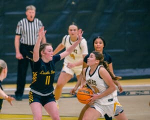 Girls' basketball game, player in white jersey attempts a shot while guarded by opponent in black jersey.