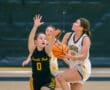 Two female basketball players in action, one attempting a shot while the other defends, indoor game setting.