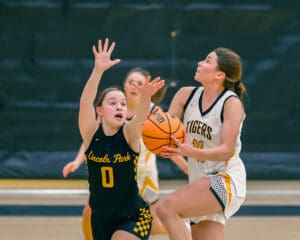 Two female basketball players in action, one attempting a shot while the other defends, indoor game setting.