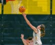Basketball player in white jersey making a layup during a game, reaching for the hoop with orange ball.