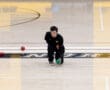 Athlete playing bocce indoors, ready to throw, focused on aiming the green ball.