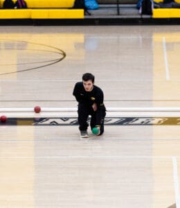 Athlete playing bocce indoors, ready to throw, focused on aiming the green ball.