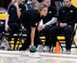 Person lining up a bocce ball shot indoors, teammates watching attentively on the sidelines.