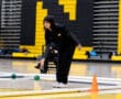 Person in sports attire participates in a bocce game in an indoor gym with yellow and black walls.
