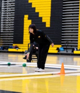 Person in sports attire participates in a bocce game in an indoor gym with yellow and black walls.