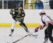Two inline hockey players face off on the rink, wearing black and white uniforms, focused on the puck.