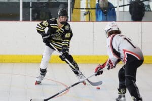 Two inline hockey players face off on the rink, wearing black and white uniforms, focused on the puck.