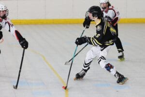 Roller hockey players in action, wearing black and white jerseys, competing on an indoor rink.