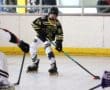 Youth roller hockey player in action, wearing black and yellow gear, competes for the puck on an indoor rink.