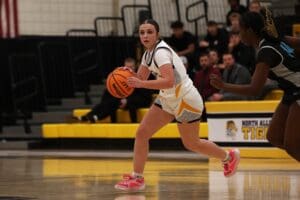 Basketball player in action, dribbling past opponent on indoor court with spectators in background.