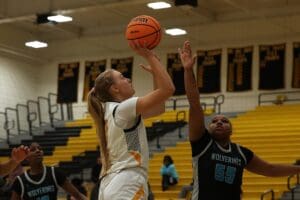 Basketball player making a jump shot while defended during a game in a gymnasium.