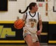 Female basketball player in white Tigers jersey dribbles the ball on the court during a game.