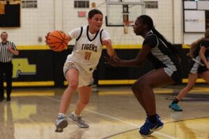 Basketball player in white jersey dribbles past a defender in black during a high school game.