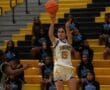 Basketball player in Tigers uniform shoots ball during game, with cheerleaders in the background on bleachers.