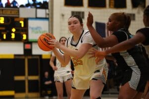 Basketball player in white jersey holds ball, defends against player in black during an intense game.