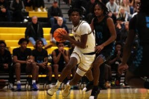 Basketball player drives to the hoop against defender during high school game, crowd watches intently.