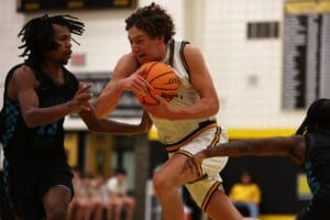 Basketball player drives through defense holding ball tightly, intense game action indoors.