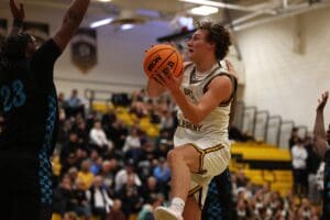 Basketball player in white uniform jumps for a shot during an intense game in a crowded gymnasium.