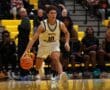 Basketball player dribbles down court during a high school game, with focused teammates and spectators watching.
