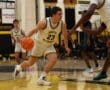 Basketball player in white jersey dribbling during a high school match on indoor court.