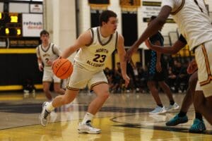 Basketball player in white jersey dribbling during a high school match on indoor court.