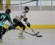 Two roller hockey players compete on an indoor rink, one wearing black and green and the other in white and yellow.