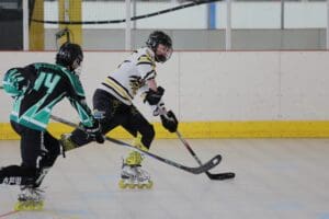 Two roller hockey players compete on an indoor rink, one wearing black and green and the other in white and yellow.
