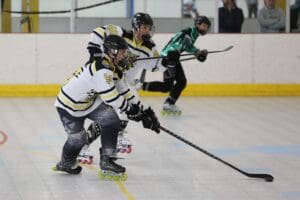 Roller hockey players in action, wearing protective gear and jerseys, competing indoors with focused determination.