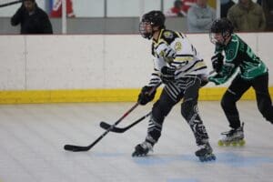 Roller hockey players in action on the rink, wearing jerseys and protective gear with sticks.