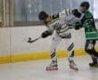 Two players in roller hockey jerseys competing during a match on an indoor rink.