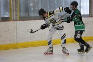 Two players in roller hockey jerseys competing during a match on an indoor rink.