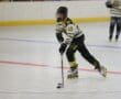 Roller hockey player in action, wearing black and yellow uniform, skating with stick on indoor rink.