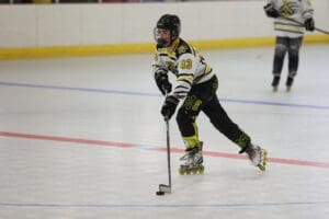 Roller hockey player in action, wearing black and yellow uniform, skating with stick on indoor rink.