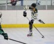 Roller hockey player in action, wearing black and white, preparing to shoot the puck on an indoor rink.