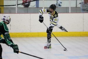 Roller hockey player in action, wearing black and white, preparing to shoot the puck on an indoor rink.