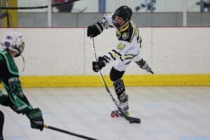 Roller hockey player in action, preparing to hit the puck during a competitive game on an indoor rink.