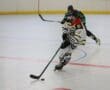 Roller hockey player in action on indoor rink, wearing a white and black uniform, controlling puck with stick.