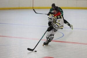 Roller hockey player in action on indoor rink, wearing a white and black uniform, controlling puck with stick.