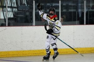 Young athlete celebrating a goal during a roller hockey game in an indoor rink.